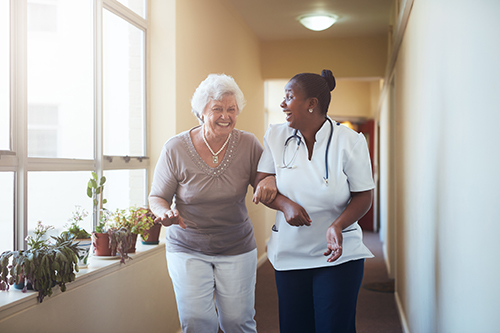 Nurse walking down the hallway with elderly woman laughing together